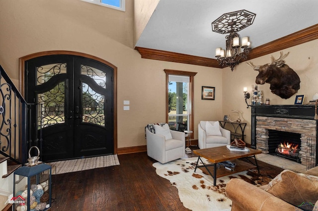 foyer entrance featuring french doors, a notable chandelier, wood-type flooring, a fireplace, and ornamental molding