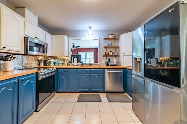 kitchen with decorative backsplash, stainless steel appliances, blue cabinets, white cabinetry, and butcher block counters