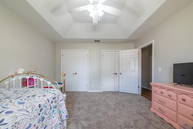 carpeted bedroom with ceiling fan, a raised ceiling, and multiple closets