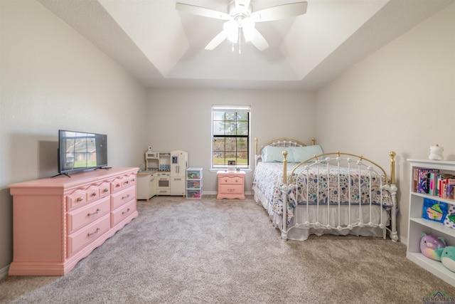 carpeted bedroom with ceiling fan and a tray ceiling