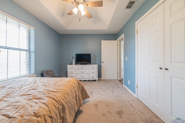 carpeted bedroom with a tray ceiling, ceiling fan, and a closet