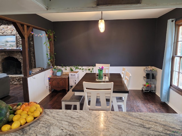 dining area featuring a stone fireplace, wood finished floors, a wainscoted wall, and a wealth of natural light