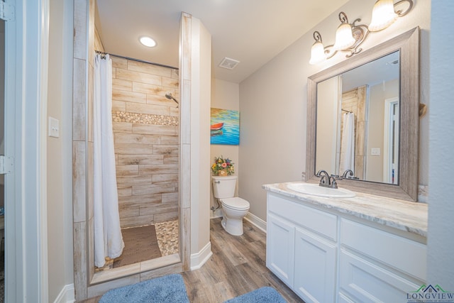 bathroom with visible vents, toilet, wood finished floors, and a tile shower