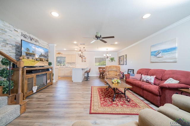 living room with light wood finished floors, ceiling fan with notable chandelier, a large fireplace, and ornamental molding