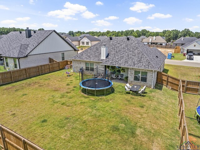 rear view of house featuring a trampoline and a yard