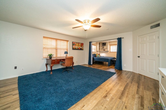 office space with a textured ceiling, ceiling fan, wood finished floors, visible vents, and baseboards