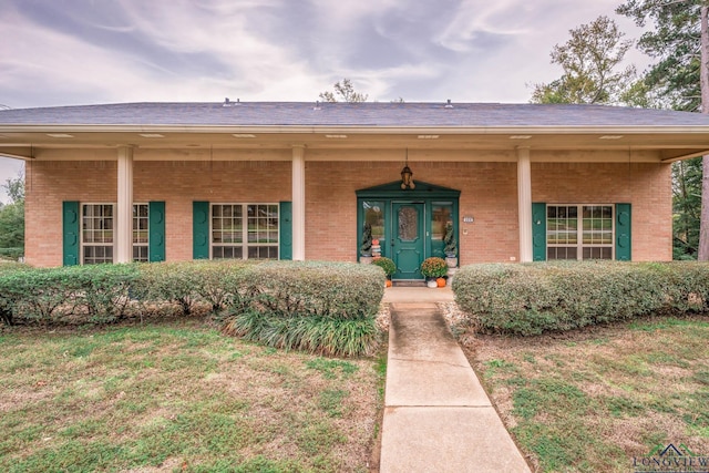 view of front of home with covered porch, brick siding, and a front lawn