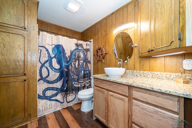 full bathroom featuring toilet, wood finished floors, vanity, and wooden walls