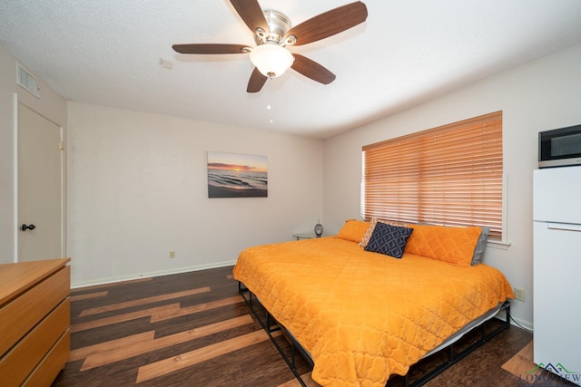 bedroom with dark wood-type flooring, ceiling fan, white fridge, and a textured ceiling