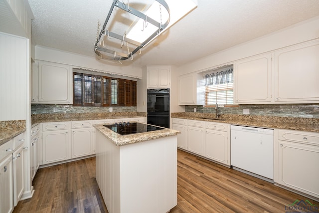 kitchen with sink, light stone counters, black appliances, a kitchen island, and white cabinets