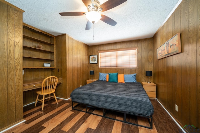 bedroom with dark hardwood / wood-style floors, built in desk, wooden walls, ceiling fan, and a textured ceiling