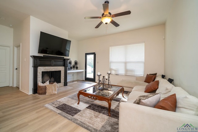 living room with a fireplace, light wood-type flooring, and ceiling fan