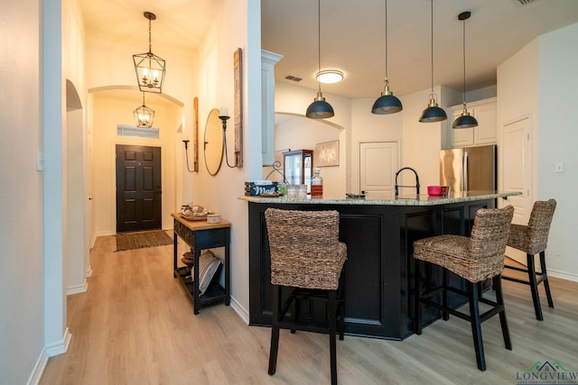 kitchen featuring stainless steel fridge, light wood-type flooring, light stone counters, white cabinetry, and hanging light fixtures