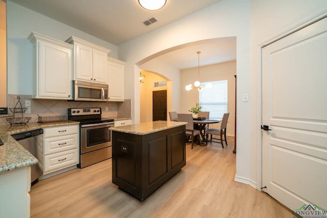 kitchen featuring light stone countertops, tasteful backsplash, light hardwood / wood-style floors, decorative light fixtures, and appliances with stainless steel finishes