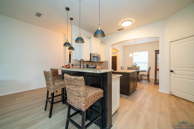 kitchen with light stone counters, a center island with sink, light hardwood / wood-style floors, and decorative light fixtures