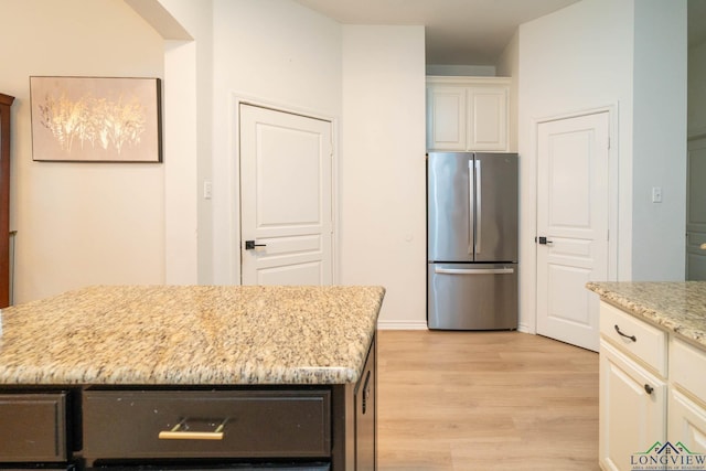 kitchen featuring light stone countertops, stainless steel fridge, white cabinets, light hardwood / wood-style floors, and a kitchen island