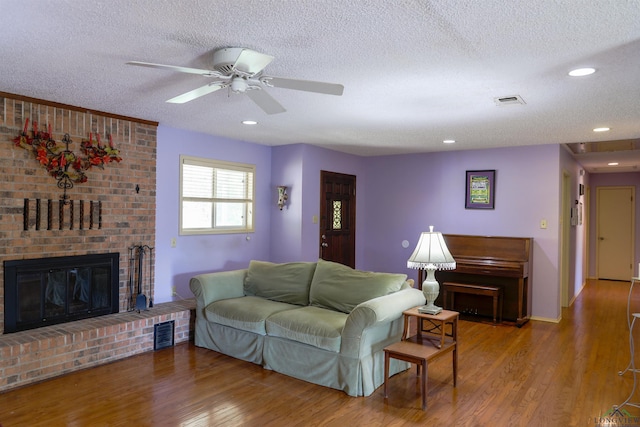 living room featuring ceiling fan, a fireplace, a textured ceiling, and hardwood / wood-style flooring