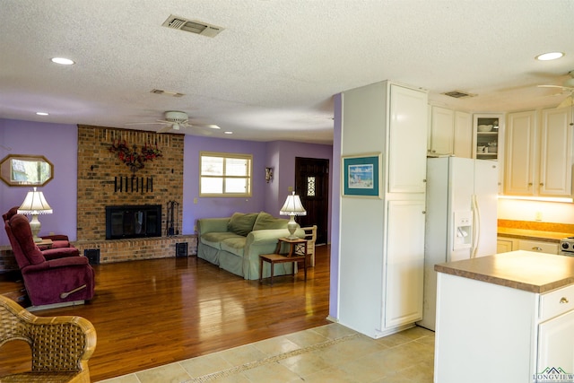 kitchen with white refrigerator with ice dispenser, white cabinets, a brick fireplace, and light tile patterned flooring