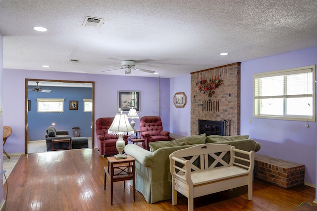 living room with ceiling fan, a fireplace, hardwood / wood-style floors, and a textured ceiling