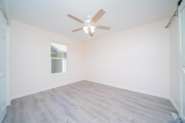 empty room featuring light hardwood / wood-style flooring, a barn door, and ceiling fan