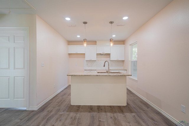 kitchen with sink, hardwood / wood-style floors, light stone counters, white cabinets, and a center island with sink