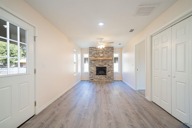 unfurnished living room featuring a stone fireplace, ceiling fan, and light wood-type flooring