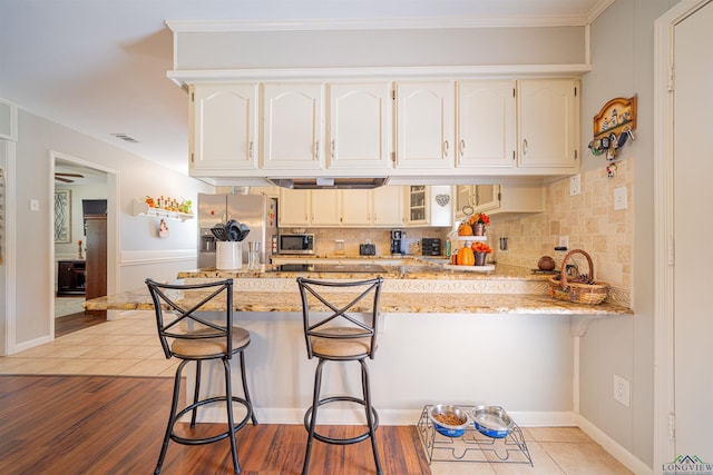 kitchen featuring a breakfast bar, white cabinetry, light stone counters, kitchen peninsula, and stainless steel appliances