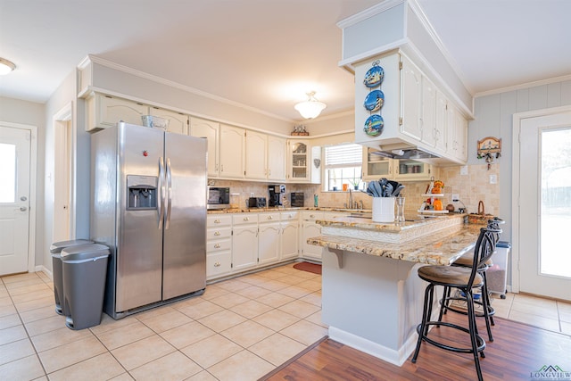 kitchen with light tile patterned flooring, white cabinetry, a breakfast bar area, kitchen peninsula, and stainless steel refrigerator with ice dispenser