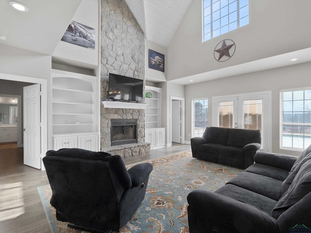 living room with built in features, a fireplace, wood-type flooring, vaulted ceiling, and french doors