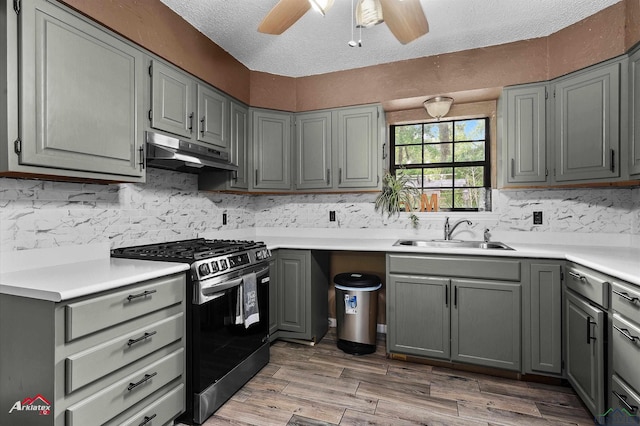 kitchen with ceiling fan, a sink, stainless steel gas range oven, gray cabinets, and under cabinet range hood