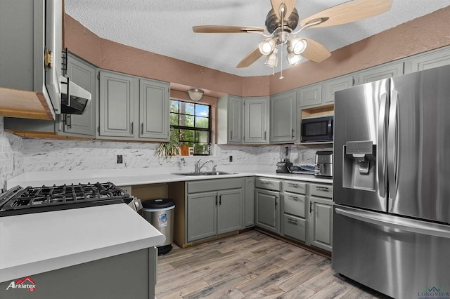 kitchen with black microwave, a sink, decorative backsplash, stainless steel refrigerator with ice dispenser, and gray cabinetry