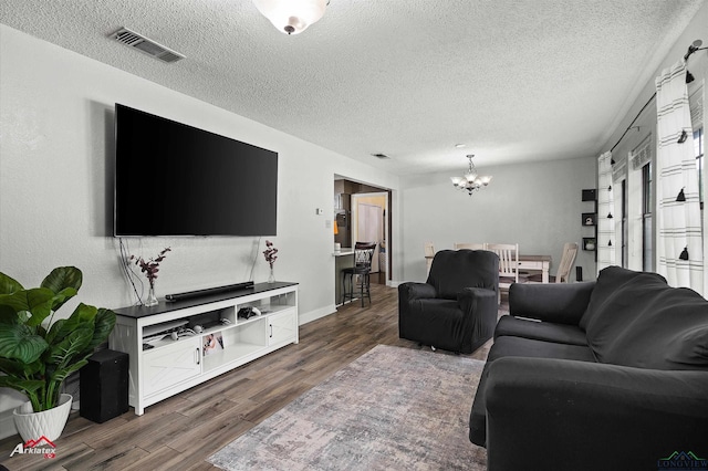 living area with a textured ceiling, a chandelier, wood finished floors, and visible vents