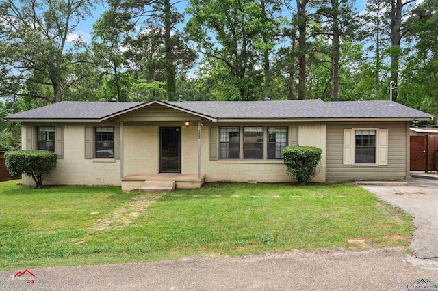 single story home with a shingled roof, a front yard, and brick siding