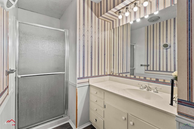 bathroom featuring a textured ceiling, a shower stall, vanity, and wallpapered walls