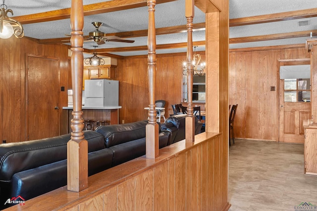 living area featuring a ceiling fan, wooden walls, beam ceiling, and a textured ceiling