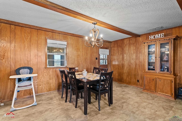 dining room with a textured ceiling, wooden walls, visible vents, beam ceiling, and an inviting chandelier