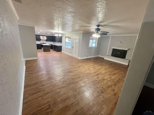 unfurnished living room featuring ceiling fan with notable chandelier, plenty of natural light, a textured ceiling, and dark wood-type flooring