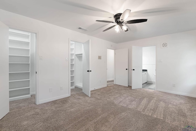 unfurnished bedroom with a closet, a walk in closet, light colored carpet, and ceiling fan