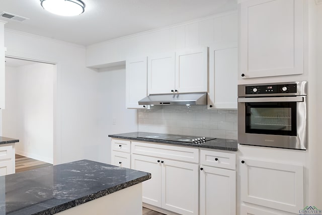 kitchen featuring black electric stovetop, backsplash, dark stone counters, stainless steel oven, and white cabinetry