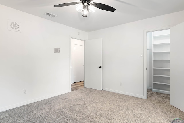 unfurnished bedroom featuring ceiling fan, a walk in closet, and light carpet