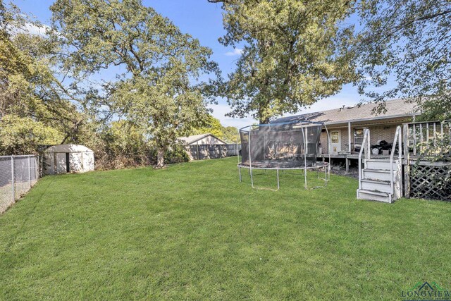 view of yard featuring a trampoline, a deck, and a storage shed