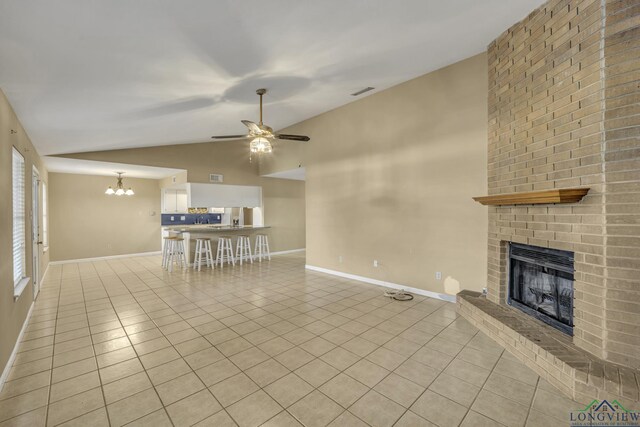 unfurnished living room featuring ceiling fan with notable chandelier, light tile patterned floors, a fireplace, and vaulted ceiling