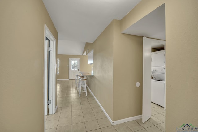 hall featuring light tile patterned flooring, lofted ceiling, and stacked washer and dryer