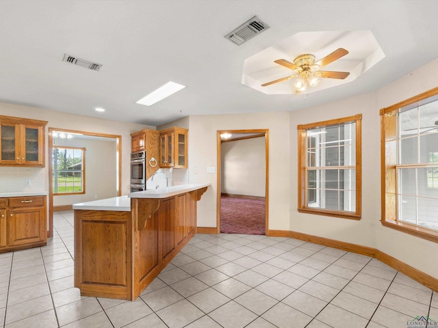 kitchen with kitchen peninsula, light tile patterned floors, ceiling fan, and a kitchen breakfast bar