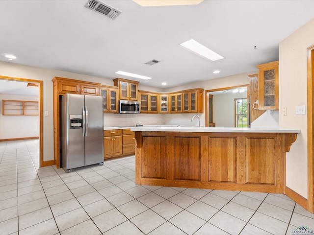 kitchen featuring kitchen peninsula, appliances with stainless steel finishes, decorative backsplash, sink, and light tile patterned floors