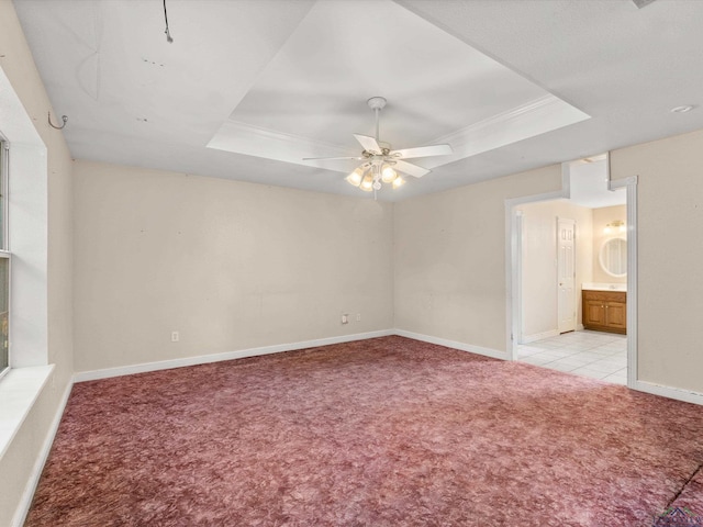 unfurnished bedroom featuring ceiling fan, a raised ceiling, ensuite bathroom, and light carpet