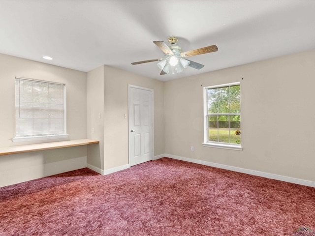 carpeted empty room featuring ceiling fan and built in desk