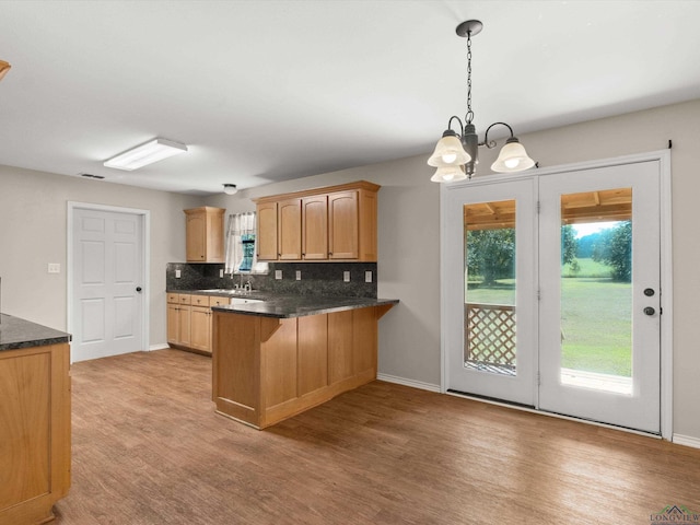 kitchen featuring kitchen peninsula, backsplash, decorative light fixtures, an inviting chandelier, and light hardwood / wood-style floors