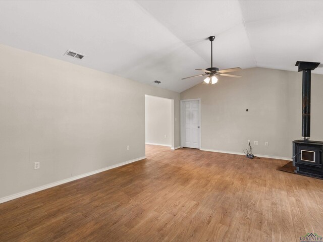 unfurnished living room with hardwood / wood-style floors, vaulted ceiling, a wood stove, and ceiling fan