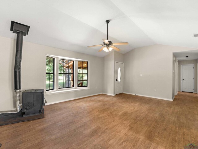 unfurnished living room with vaulted ceiling, hardwood / wood-style flooring, a wood stove, and ceiling fan